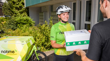 Zufriedene Velokurierin von notime übergibt Paket an einen Kunden.