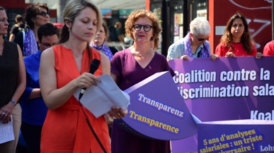 Mehrere Personen mit lila Schildern kämpfen für Gleichstellung beim Lohn und stehen am Bern Bahnhof