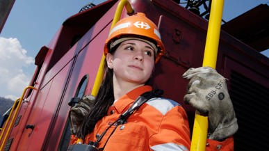 SBB Mitarbeiterin in Oranger Arbeitskleidung auf einem roten Güterzug.