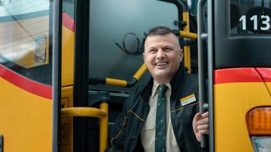 Ein Postauto-Mitarbeiter, der bei der Eingangstreppe eines Postautos sitzt und lacht