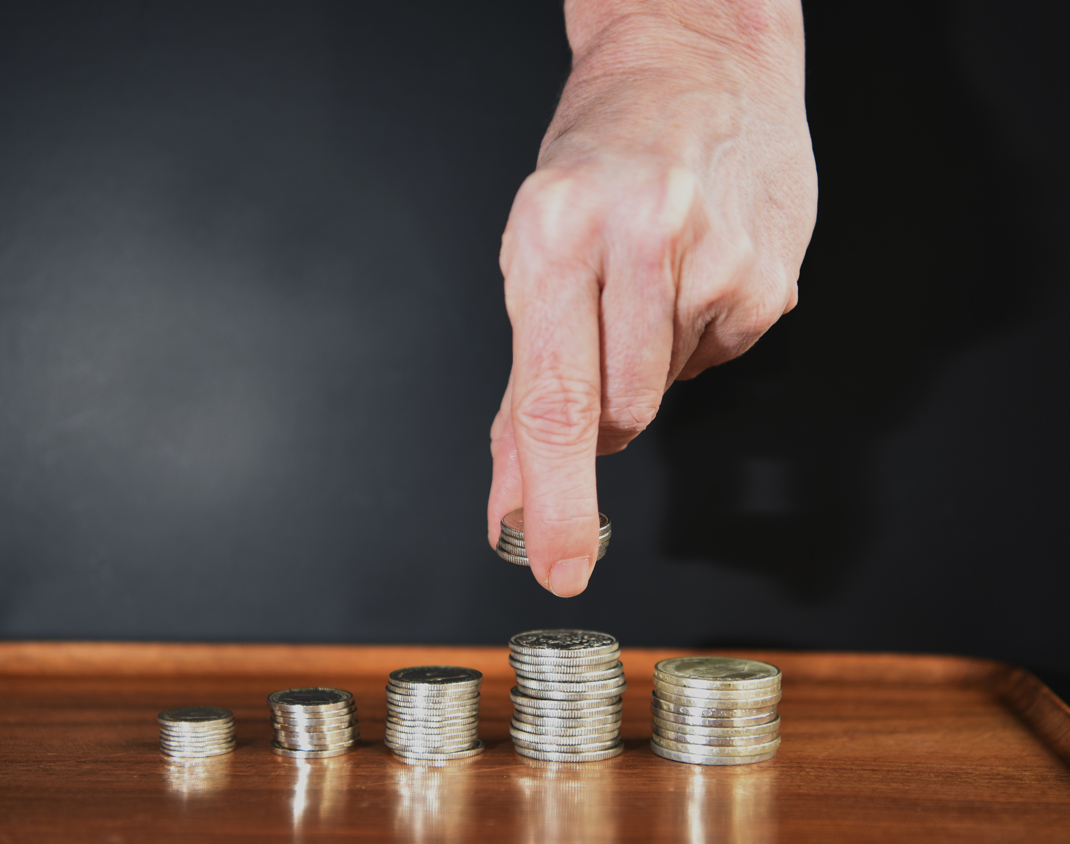 Eine Hand legt eine Münze auf einen Münzstapel