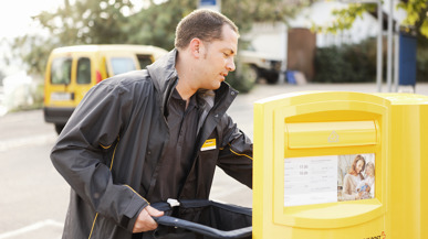 Ein Post-Mitarbeiter leert einen gelben Briefkasten