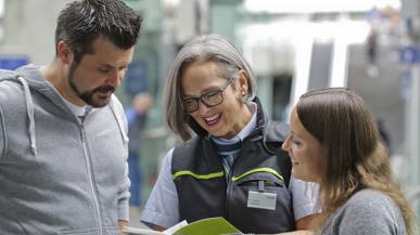 Eine BLS-Reisebegleiterin berät einen Kunden und eine Kundin mit einem BLS-Prospekt in den Händen
