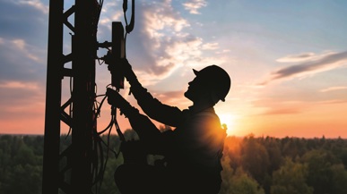 Ein Techniker, der bei Sonnen auf oder Untergang einen Handymast erklimmt