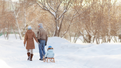 Mutter, Vater und Kind auf dem Schlitten auf einem verschneiten Weg