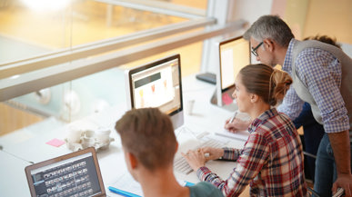 Zwei Lehrnende an Laptops mit Ausbildner